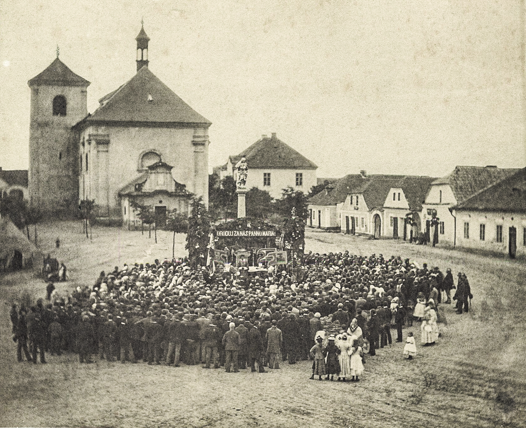 Říčanské náměstí během církevní slavnosti v roce 1878. Starý, ještě přízemní dům čp. 65 vidíme úplně vpravo.